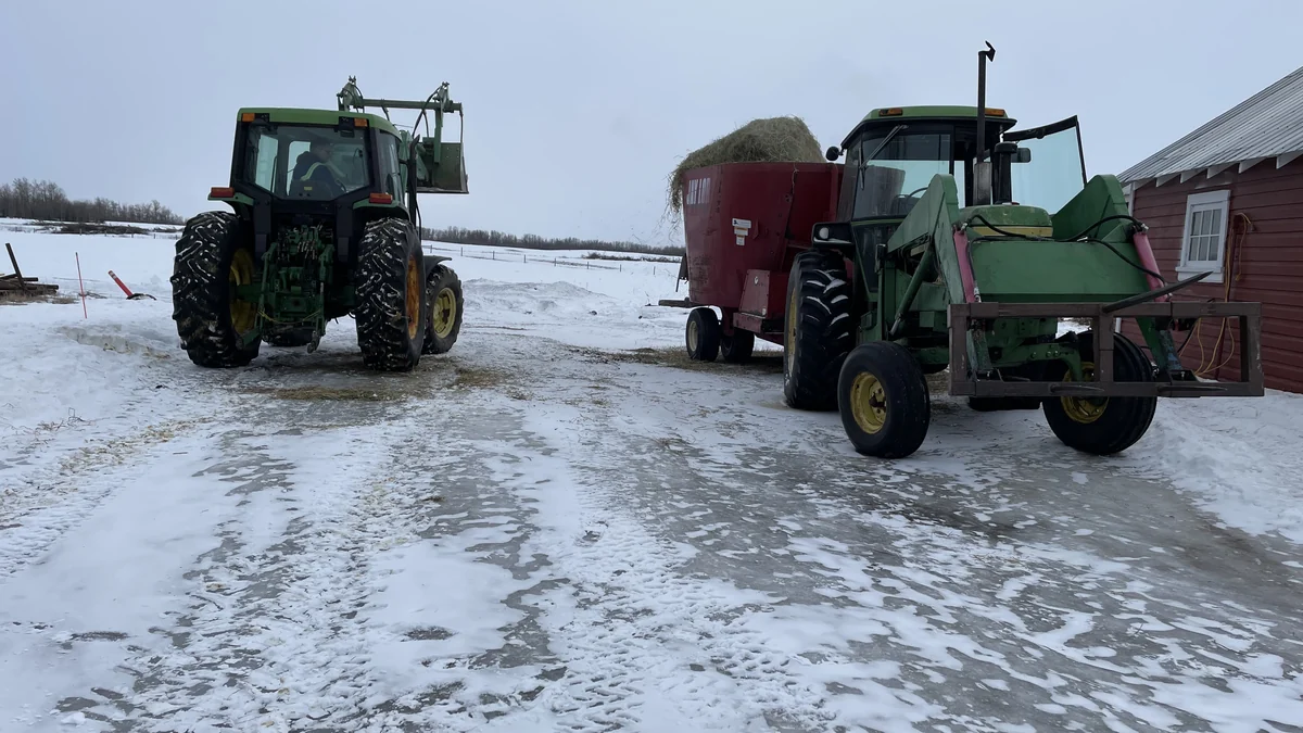Two tractors and a feed mixer in a snowy farmyard.