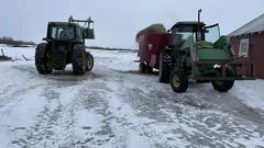 Two tractors and a feed mixer in a snowy farmyard.